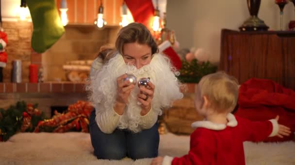 一个正面的白人女人在圣诞舞会上玩耍 摘下圣诞老人的胡子 与坐在地毯上的女婴交谈的画像 快乐而轻松的母亲和女儿在家里度假 — 图库视频影像