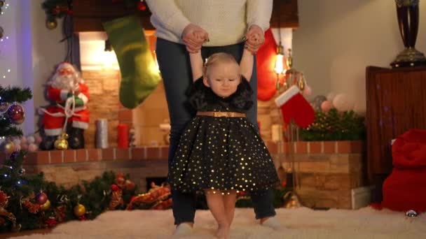 前看漂亮的女婴在做衣服的步伐与难以辨认的女人牵着手 新年前夕 快乐可爱的白人小孩在家里客厅里散步 — 图库视频影像