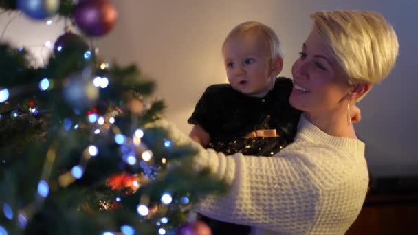 Χαμογελαστή Γυναίκα Και Ενθουσιασμένο Κοριτσάκι Θαυμάζοντας Χριστουγεννιάτικα Στολίδια Στο Δέντρο — Αρχείο Βίντεο
