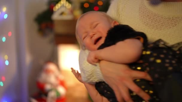 在圣诞灯的背景下 白人女性手中哭泣的女婴的画像 除夕之夜 穿着黑色衣服的不满意的幼儿在家里大声叫喊 慢动作 — 图库视频影像