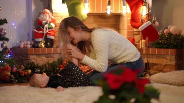 在客厅的壁炉边 一个笑着的女人在慢慢地和迷人的女婴玩耍 纵观爱白种人的母亲与女儿共度圣诞的美景 — 图库视频影像