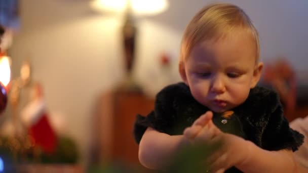 婴儿在室内圣诞树上伸展成圣诞玩具的肖像 与难以辨认的母亲共度佳节前夕 身穿黑衣的库里奥斯白人女孩在家里 — 图库视频影像