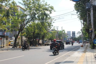 Sokaklar araçlarla dolu. Yanlarında ağaçlar ve kaldırımlar var.