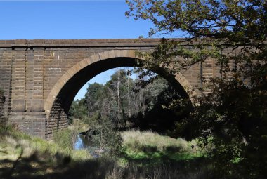 Old historic stone arch bridge against the background of blue sky and trees