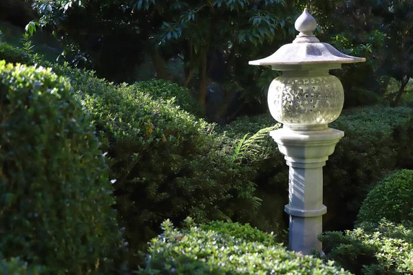 Bahçede yeşil dalların arasında oyulmuş beyaz taş fener, güzel bahçe dekorasyonu ayrıntıları.