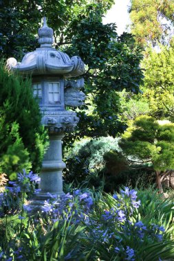 Yeşil ağaçların ve manzaraların arasındaki bir parktaki taştan Japon feneri.