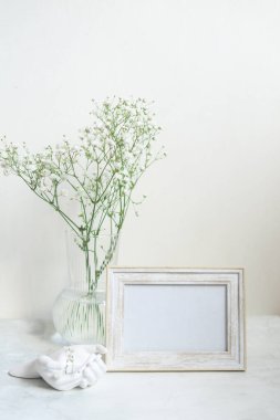Ahşap masada beyaz portre çerçevesi modeli. İçinde gypsophila.candinavian iç tasarımı olan modern seramik vazo.