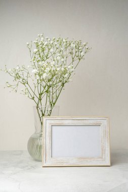 Ahşap masada beyaz portre çerçevesi modeli. İçinde gypsophila.candinavian iç tasarımı olan modern seramik vazo.