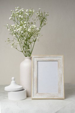 Ahşap masada beyaz portre çerçevesi modeli. İçinde gypsophila.candinavian iç tasarımı olan modern seramik vazo.