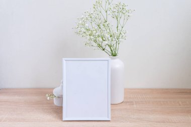 Ahşap masada beyaz portre çerçevesi modeli. İçinde gypsophila.candinavian iç tasarımı olan modern seramik vazo.