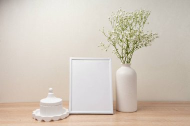 Ahşap masada beyaz portre çerçevesi modeli. İçinde gypsophila.candinavian iç tasarımı olan modern seramik vazo.
