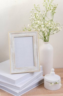 Ahşap masada beyaz portre çerçevesi modeli. İçinde gypsophila.candinavian iç tasarımı olan modern seramik vazo.