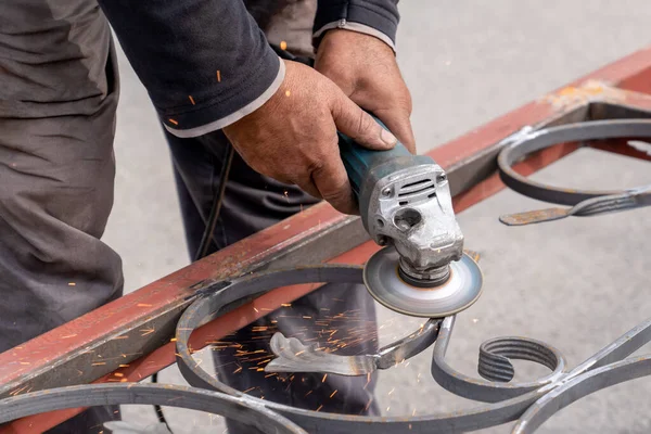 Man grinds metal with angle grinder in metal workshop. Sparks fly on the sides. — 图库照片