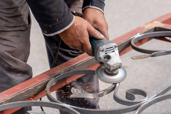 Metal öğütücüyle metal atölyesinde öğütüyor. Yanlarda kıvılcımlar uçuşuyor.