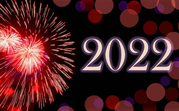 Gott nytt år 2022, festliga röda fyrverkerier på bakgrund svart himmel med bokeh och kopiera utrymme. Stockfoto