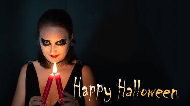Cadılar Bayramı kavramı. Cadı suretindeki bir kız, elinde yanan mumla doğrudan çerçeveye bakar. Üzerinde 