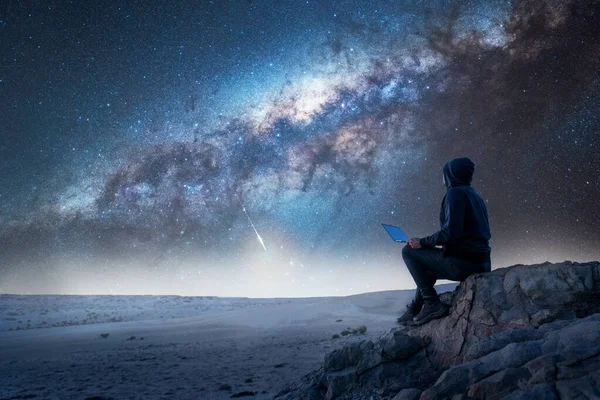 一个人坐在山顶上 晚上带着笔记本电脑凝视着银河的轮廓 — 图库照片