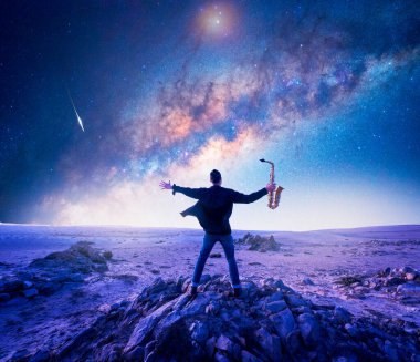 Şili 'nin Atakama Çölü' nde, Samanyolu 'nun altındaki bir kayanın üzerinde açık kolları olan bir müzisyen ya da saksafoncunun silüeti.