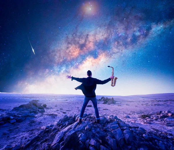 Şili 'nin Atakama Çölü' nde, Samanyolu 'nun altındaki bir kayanın üzerinde açık kolları olan bir müzisyen ya da saksafoncunun silüeti.