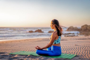 Latin kadın meditasyon yapıyor ya da gün batımında plajda yoga yapıyor.