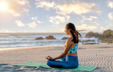 Latin genç kadın meditasyon yapıyor ya da gün batımında plajda yoga yapıyor.