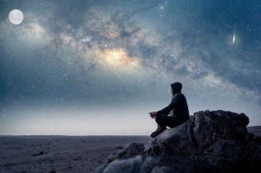 Dağın tepesinde oturmuş, yıldızlı geceyi Atacama Çölü 'nde Samanyolu ve Ay' la meditasyon yapıyor ya da tasarlıyor.