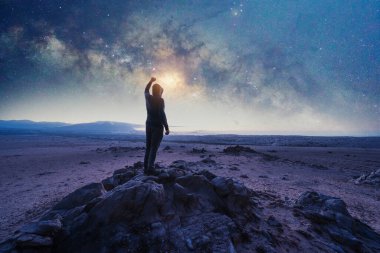 Kayanın üzerinde duran adam, arkasını gören, elini kaldırıp Samanyolu 'na bakan ve okyanusun üzerindeki yıldızlara bakan adam.