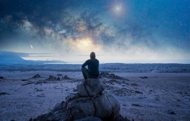 Kaya üzerindeki insan geceleri Samanyolu 'nun altında meditasyon yapıyor ya da dua ediyor ve yıldız kayıyor.