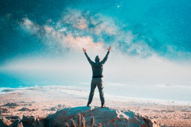 Gece vakti, Samanyolu ve okyanus altyapısı ile el kaldırarak dağın tepesinde duran bir insanın silüeti.