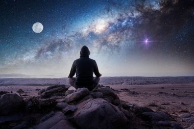 Bilinmeyen kişi geceleri dışarıda, dağın tepesinde, Samanyolu ve Ay 'ın arka planında meditasyon yapıyor.