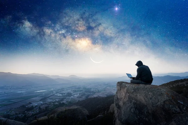 一个带着笔记本电脑和银河系背景坐在山顶上的人的轮廓 — 图库照片
