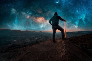 Adam dağın tepesinde duruyor. Samanyolu 'nun altında ışık var.