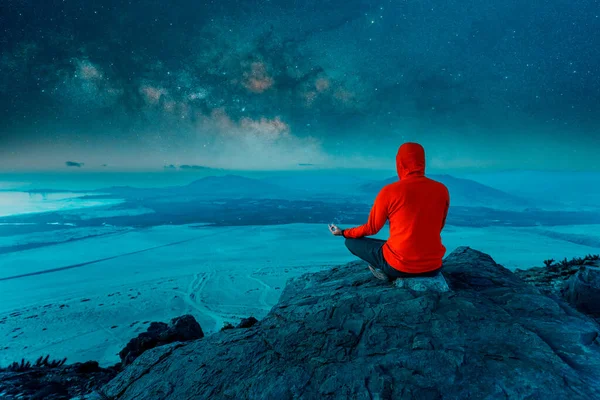unknown person sitting on the top of the mountain meditating or contemplating horizon over the ocean with Milky Way background, back view