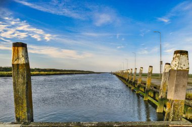 Issız bir liman boyunca eski, yıpranmış demirleme direkleri. Hollanda 'daki de Wadden Denizi' ndeki Noordpolderzijl 'in gelgit limanı boyunca, algalarla kaplı eski demirleme noktaları.