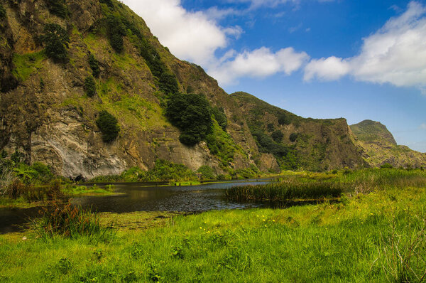 Small lake at the foot of high, rocky hills in a wetland near Tunnel Point and Zion Hill, close to Karekare in the Waitakere Ranges, Auckland, New Zealand. 