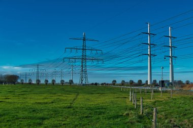 Geleneksel ve modern elektrik direkleri Hollanda 'nın Groningen eyaletinde yeşil bir alan.