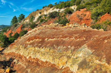 Cerro de Vilarinha, Algarve, Portekiz 'de Akdeniz çalılıklarıyla kaplı, kırmızı, sarı ve beyaz kayaların triasik tortu tabakaları. 