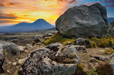Yeni Zelanda 'daki Ngauruhoe Dağı, Yüzüklerin Efendisi' nden Kıyamet Dağı, dramatik bir akşam gökyüzünün altında, ön planda dev bir kayayla.