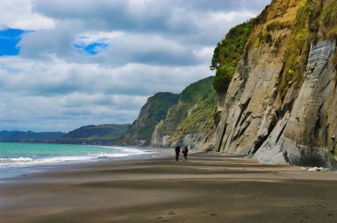 Issız bir sahilde yüksek kireçtaşı kayalıklarıyla yürüyen iki kişi. Whitecliffs, Taranaki bölgesi, Kuzey Adası, Yeni Zelanda. 