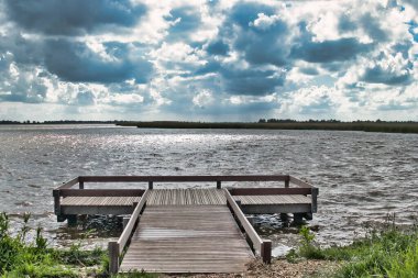 Göl kenarındaki küçük ahşap iskele, tepemizde yağmur bulutları ve suda yansıyan güneş.