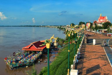The boulevard along the Mekong River in Nong Khai, Thailand, with a large restaurant boat moored at the quay, on a sunny day.