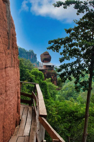 Narrow wooden walkway high on the steep rock face the temple and meditation centre Wat Phu Tok (Wat Chetiya Khiri Wihan), province of Bueng Kan, Thailand, with a view of the northeastern shrine