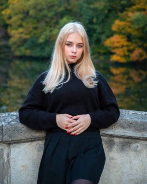 Nehir ve ağaçlarla sonbahar parkında poz veren kız