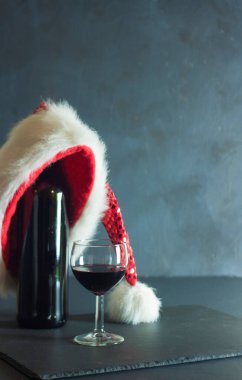 Bir şişe kırmızı şarap ve bir bardak. Kırmızı şarap bardağa dökülüyor. Şarabın üstünde Noel Baba şapkası