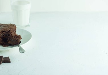 Chocolate brownie with a spoon in a plate. A glass of milk in the background