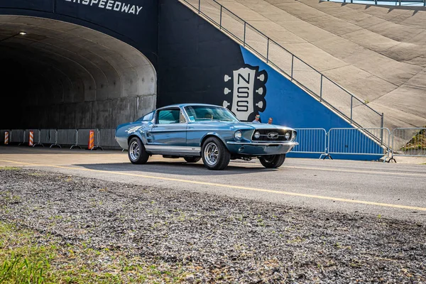 Lebanon, TN - May 14, 2022: Wide angle front corner view of a 1967 Ford Mustang GT Fastback driving on a road leaving a local car show.