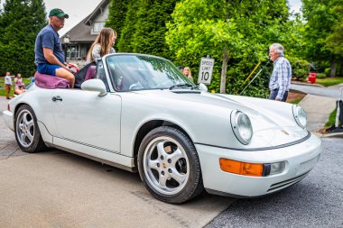 Highlands, NC - June 10, 2022: High perspective front corner view of a 1991 Porsche 911 Carrera 4 Cabriolet driving on a road leaving a local car show.