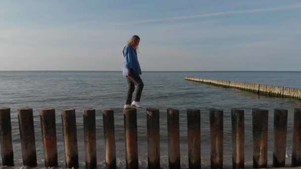 Mujer joven caminando sobre rompeolas de madera en la playa, Mar Báltico, tiro aéreo — Vídeos de Stock