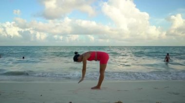 Pembe takım elbiseli genç kadın deniz kenarında gün doğumunda plajda yoga yapıyor..