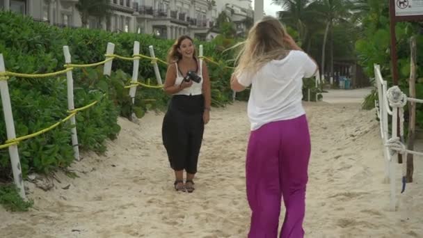Jovem mulher de calças rosa posando para um fotógrafo rindo na praia — Vídeo de Stock